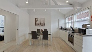 A modern kitchen with white cabinets, a dining table with chairs, and a large window with blinds.