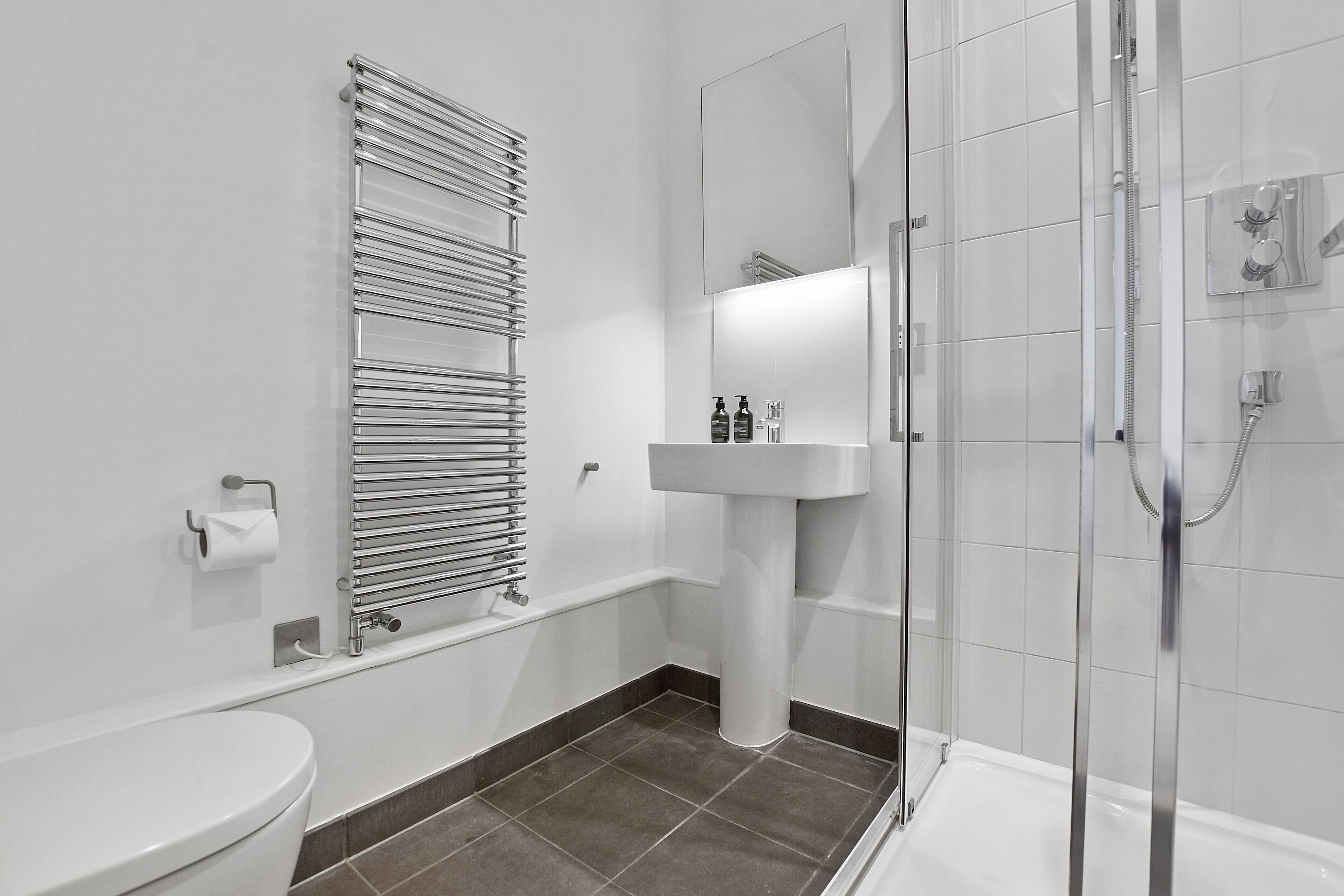 A modern bathroom with a toilet, a towel rack, a sink, and a shower area.