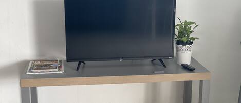 A flat-screen TV on a wooden table with a remote control and a magazine.