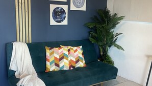 Un divano color petrolio con cuscini colorati, una coperta bianca e una parete con tre opere d'arte incorniciate.