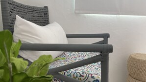 Una sedia in vimini con un cuscino decorato, un cuscino bianco e un poggiapiedi intrecciato.