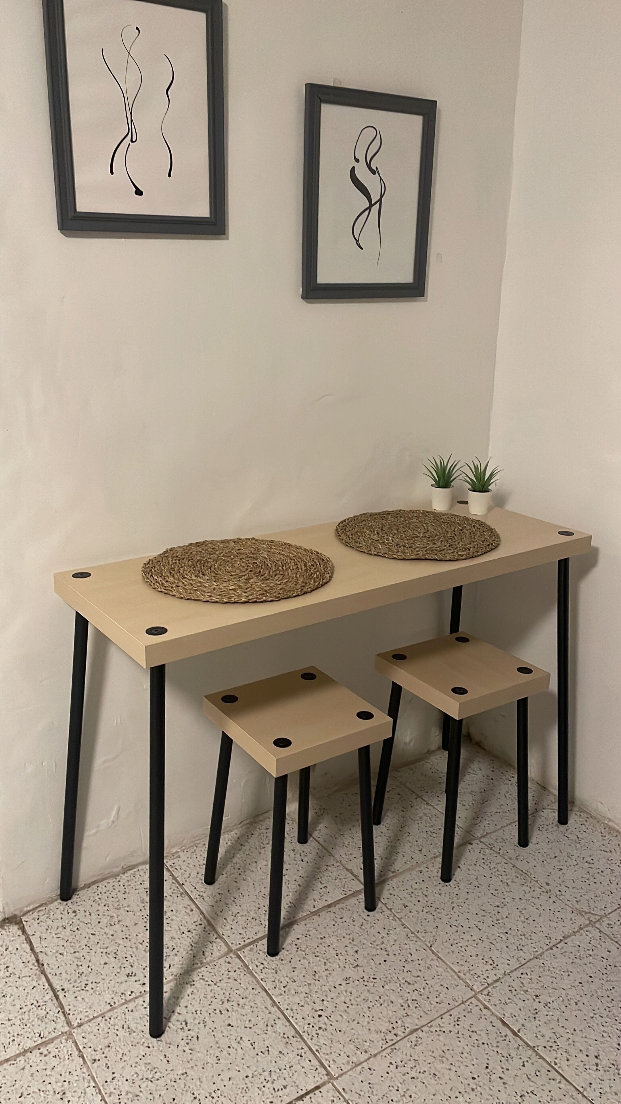 Une table minimaliste agrémentée de sets de table tissés, de deux œuvres d’art abstraites encadrées et de petites plantes en pot.