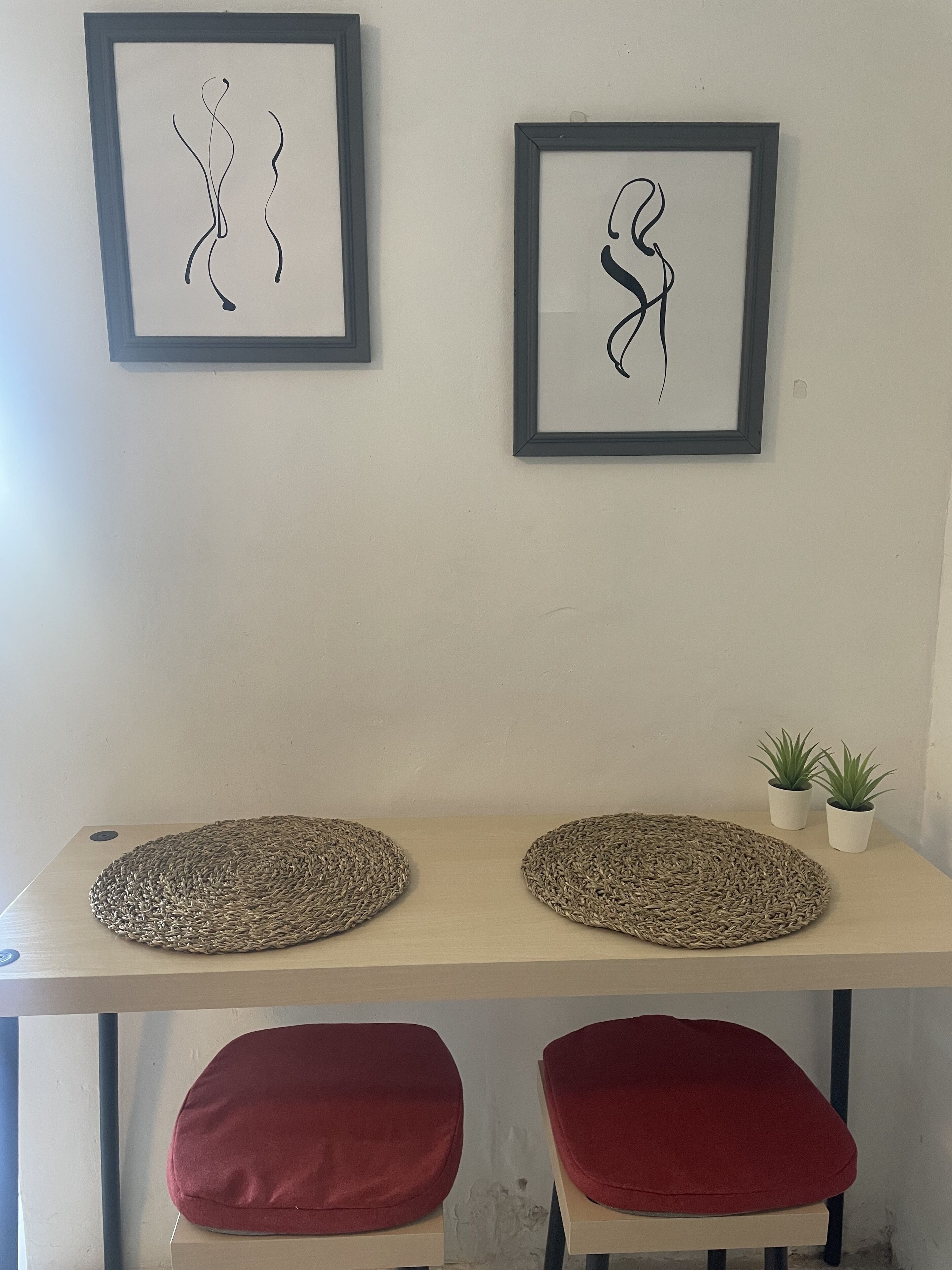 A room with two framed abstract artworks, a woven placemat, a small potted plant, and red cushioned seating.