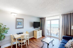 Relax in a spacious room with a sofa, dining table, and flat-screen TV, offering a view of the beach.