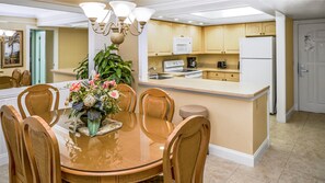 A modern kitchen with wooden cabinets, a central island, and a dining area with a glass table and wicker chairs.