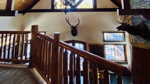 A wooden interior with a high ceiling, a chandelier, and a mounted deer head.