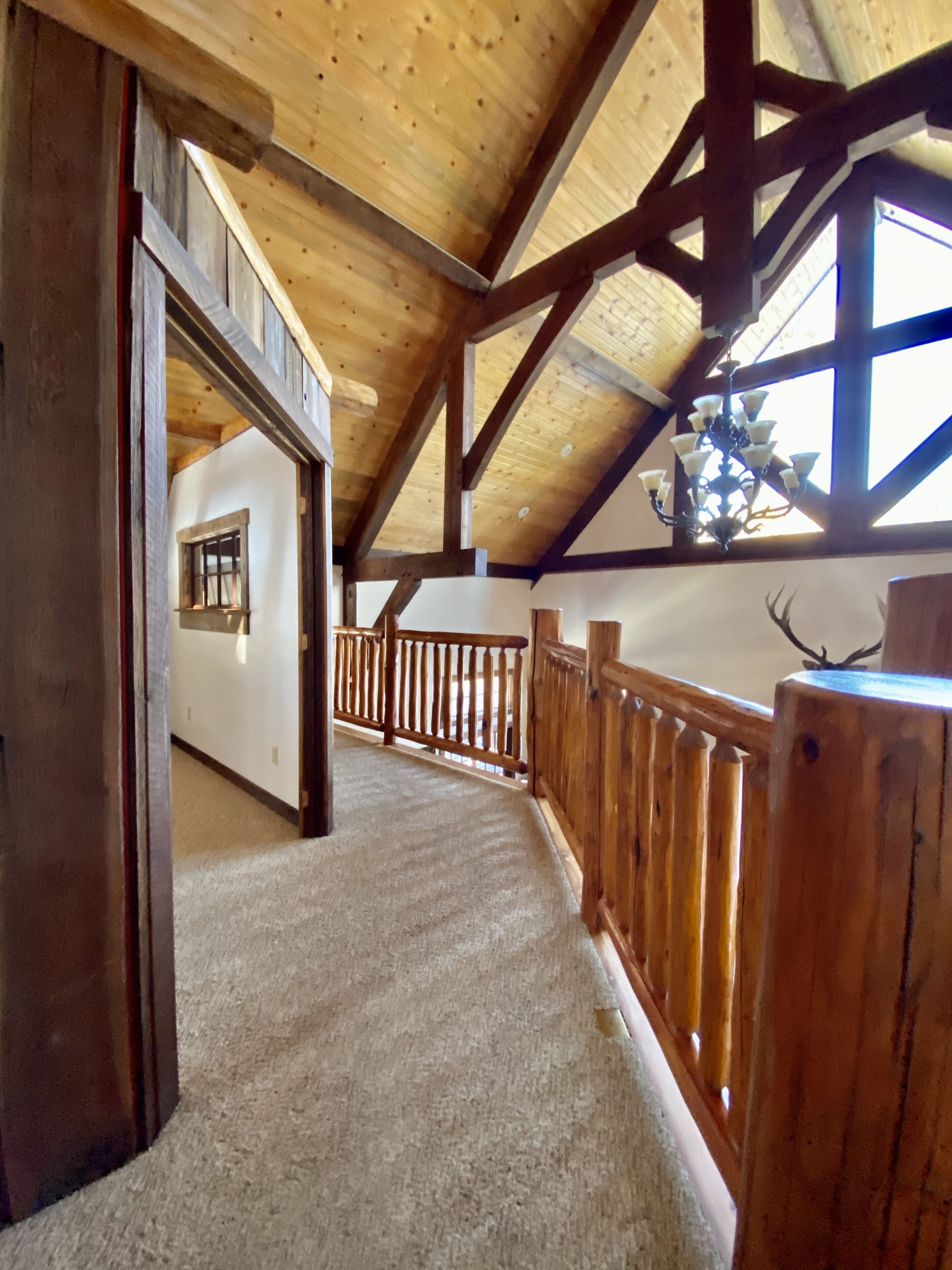 A wooden interior with a high ceiling, a balcony with a railing, and a view of the outdoors.