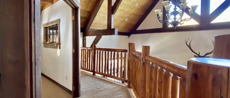 A wooden interior with a high ceiling, a balcony with a railing, and a view of the outdoors.