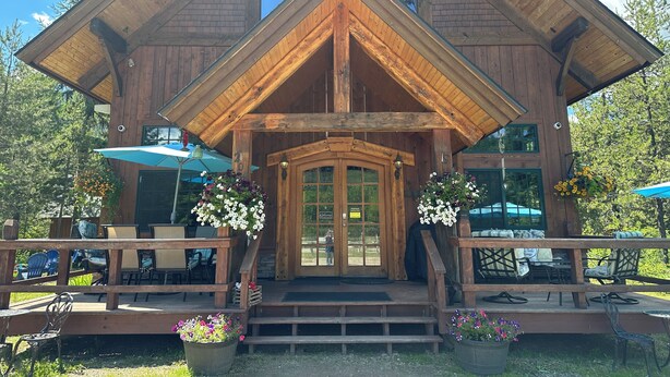 A wooden lodge with a large entrance, outdoor seating, and flower arrangements.
