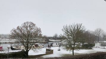 A snow-covered landscape with a bridge, trees, and a body of water.