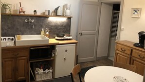 Cocina compacta con lavaplatos, estufa, microondas y refrigerador. Incluye una pequeña mesa de comedor y una silla.