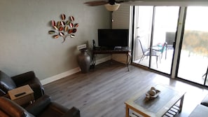 A living room with a TV, a decorative metal wall piece, a vase, and a sliding glass door leading to an outdoor area.
