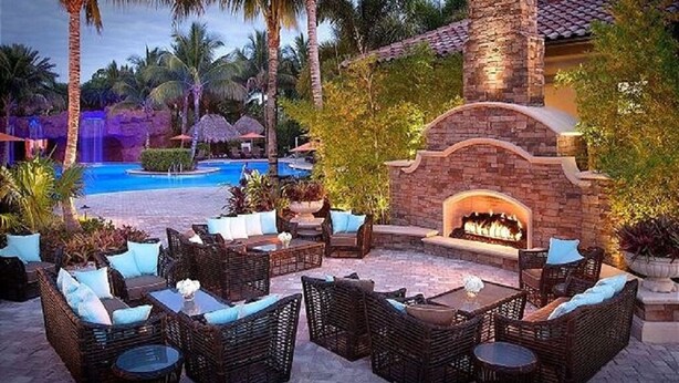 An outdoor lounge area with wicker furniture, a pool, and a stone fireplace.