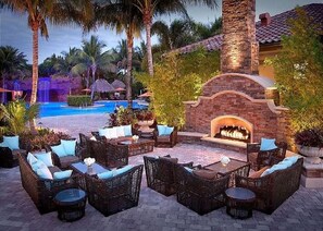 An outdoor lounge area with wicker furniture, a pool, and a stone fireplace. - Elegant, Immaculate, Pristine. 2500 SqFt 3Br Estate Home. Lots of Wow Factor. (Naples)