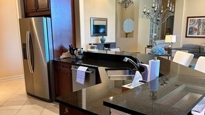 A modern kitchen with a central island, stainless steel refrigerator, and a dining area with a chandelier.