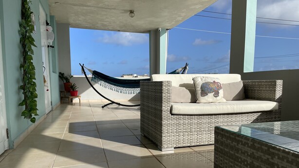 A balcony with a wicker sofa, a hammock, and a glass table. - studio apartment near to airport (Carolina)
