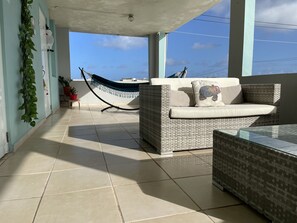 Un balcon avec un canapé en osier, un hamac et une table en verre.