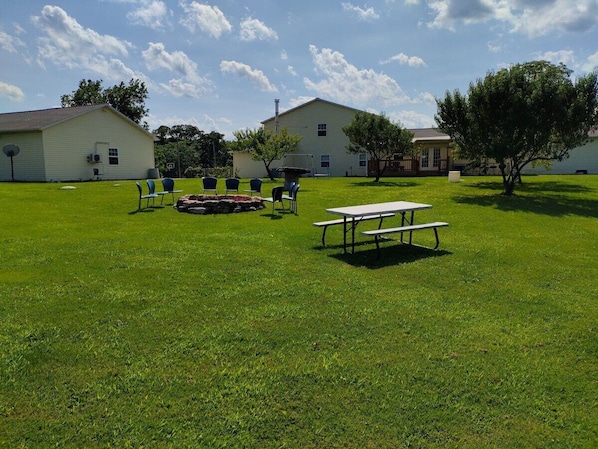 A grassy outdoor area with picnic tables and chairs, surrounded by buildings.