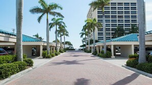 A hotel corridor with palm trees, a clear sky, and a building with a blue roof.