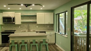 Una cocina con armarios blancos, un microondas de acero inoxidable, un fregadero y una isla grande con taburetes de bar.