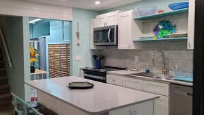 Una cocina moderna con armarios blancos, un microondas, una estufa y un fregadero. Hay una escalera que conduce a otra habitación.
