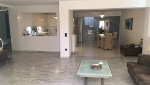 A spacious living area with a glass-top coffee table, a brown sofa, and a dining area with a table and chairs. - Stunning 4-bed Villa in Lagonisi Kalivia Thorikou (Saronikos)