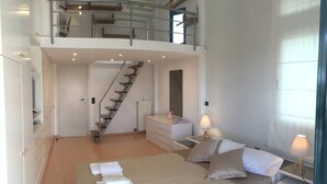 A bedroom with a bed, bedside tables, a dresser, a mirror, and a staircase leading to an upper level. - Stunning 4-bed Villa in Lagonisi Kalivia Thorikou (Saronikos)