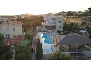 A residential area with a swimming pool, houses, and a hilly landscape in the background.