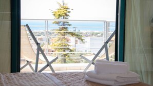 A bed with a view of a balcony, a window with a view of a tree and buildings, and a stack of towels on the bed. - Stunning 4-bed Villa in Lagonisi Kalivia Thorikou (Saronikos)