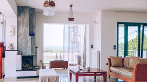 A modern living room with a fireplace, a sofa, a coffee table, and a view of the outdoors. - Stunning 4-bed Villa in Lagonisi Kalivia Thorikou (Saronikos)