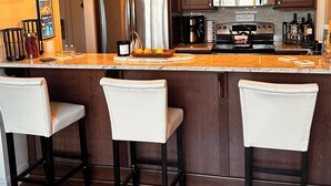 Una cocina moderna con una isla central, taburetes de bar, electrodomésticos de acero inoxidable e iluminación colgante.