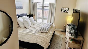 Un dormitorio con una cama grande, una mesita de noche, un espejo y una ventana con cortinas.