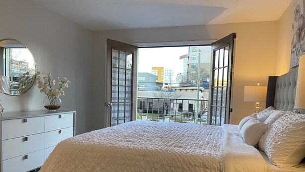Une chambre avec un grand lit, une commode, un miroir et une vue sur la ville, grâce à des portes ouvertes.