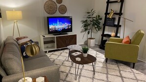 Un salon moderne comprenant un canapé, une table basse, un téléviseur, des œuvres d’art décoratives accrochées au mur, une plante et une bibliothèque.