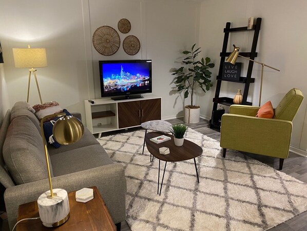 A modern living room with a sofa, a coffee table, a TV, decorative wall art, a plant, and a bookshelf. - Furnished Condo next to St Thomas Hospital (Nashville)