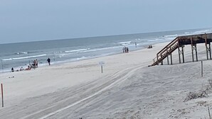 Ein Strand mit einer Holzsteg und einem Schild, das eine Rettungswache anzeigt.