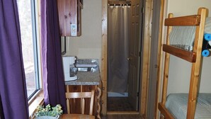 A compact room with a wooden table, a bunk bed, and a shower area. - NEW!  Village of Hope - Cabin #12 (Ava)