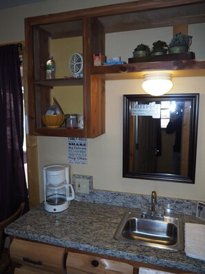 A kitchen with granite countertops, a coffee maker, a sink, and a framed family rules sign. - NEW!  Village of Hope - Cabin #12 (Ava)