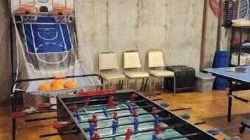 Una habitación con mesa de futbolín, sillas y aro de baloncesto.