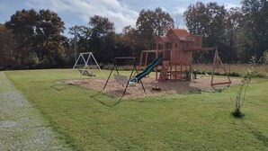 A playground with a wooden playhouse, swings, and slides. - NEW!  Village of Hope - Cabin #12 (Ava)