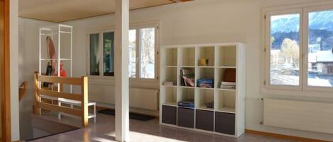 Una habitación amplia con techo de madera, ventanas grandes y una estantería empotrada.