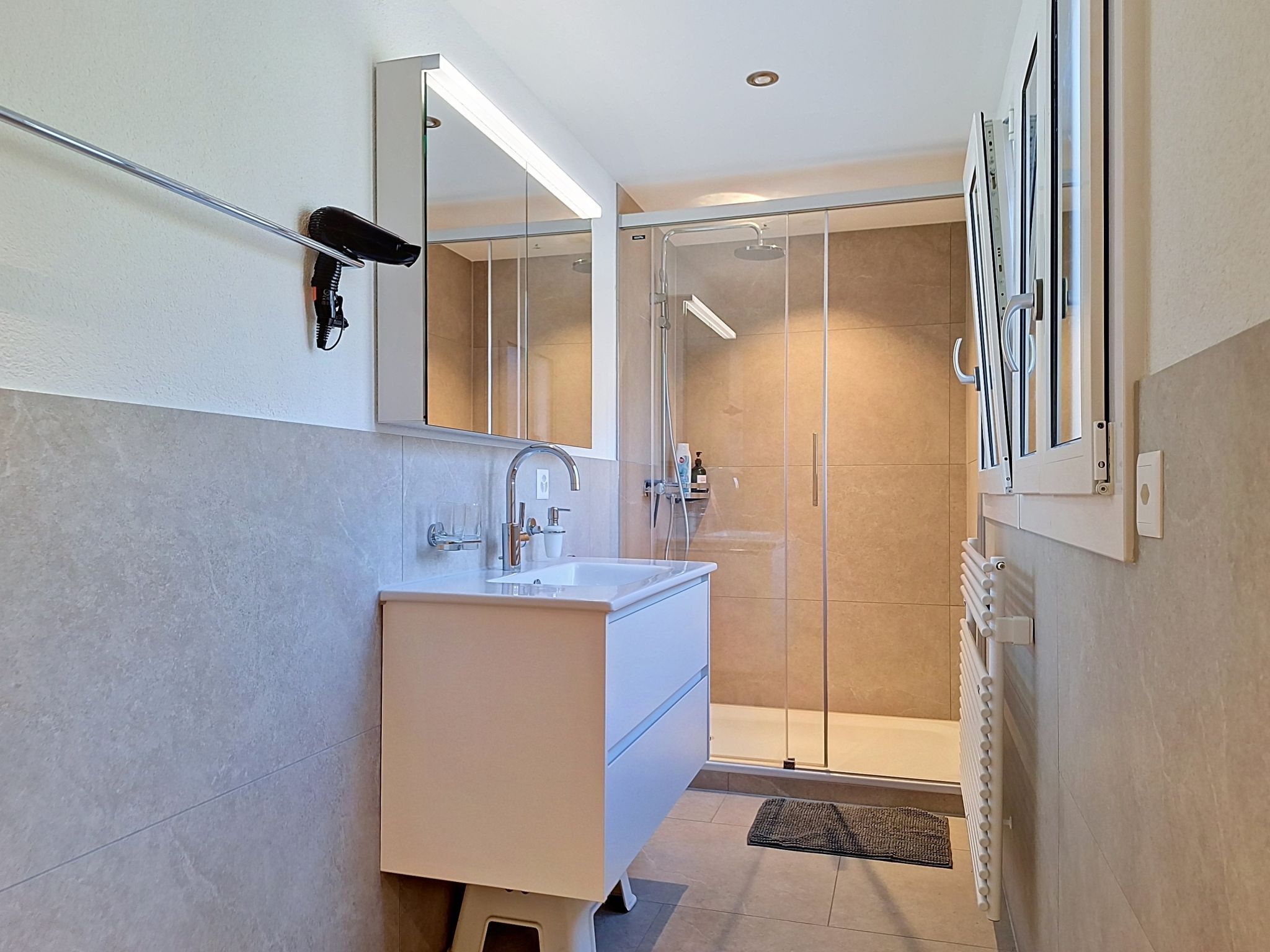 A modern bathroom with a white vanity, a glass shower enclosure, and a mirror above the sink.