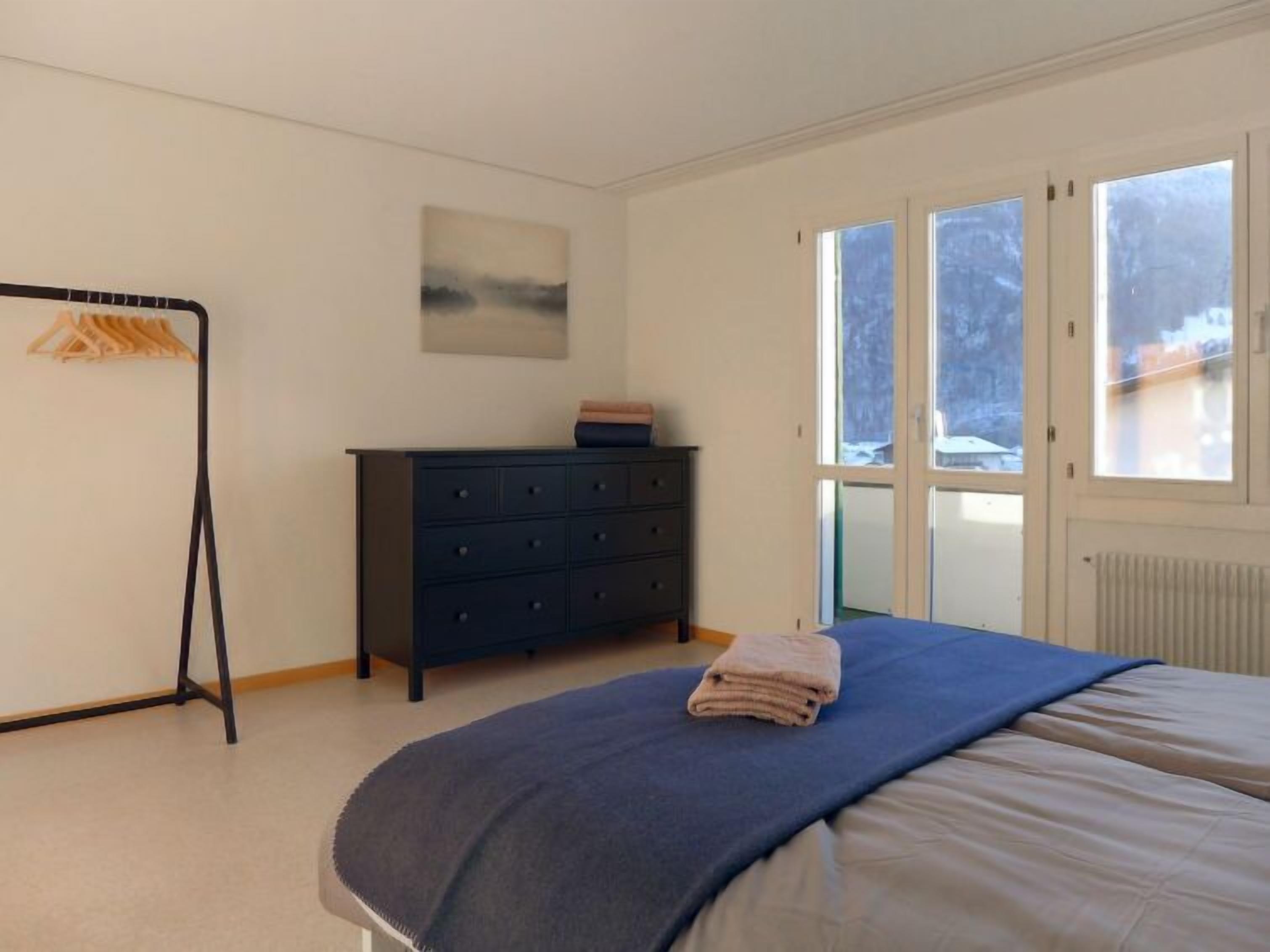 Une chambre à coucher avec un lit, une commode, une fenêtre et un radiateur.