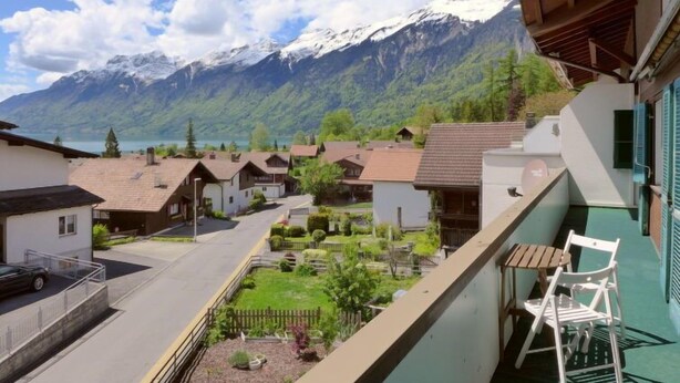 Ein Wohngebiet mit Häusern, einem Balkon mit Tisch und Stühlen sowie einer Bergkulisse.