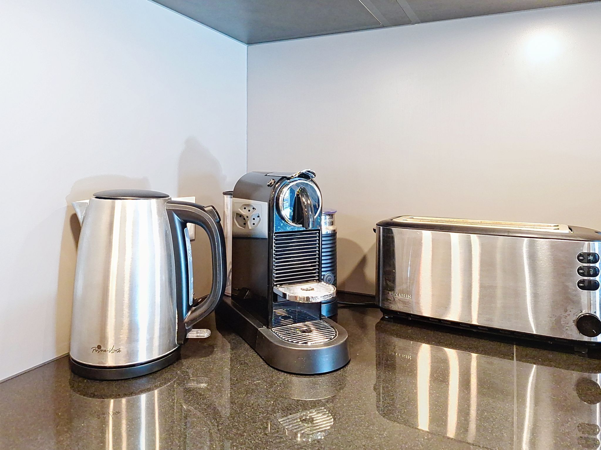 Una kitchenette con hervidor de acero inoxidable, cafetera y tostadora.