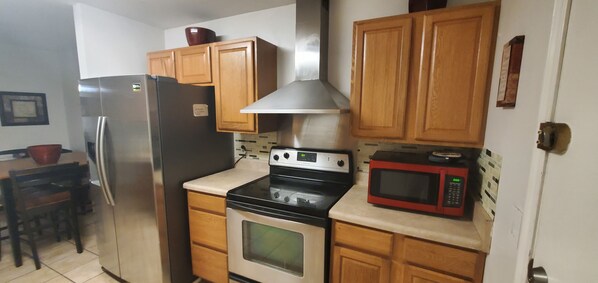 A kitchen with wooden cabinets, a stainless steel refrigerator, a black oven, and a red microwave. - Welcoming Quaint Home (Stone Mountain)