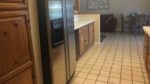 Una cucina con mobili in legno, un frigorifero in acciaio inossidabile, una lavastoviglie e un pavimento piastrellato.