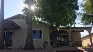 Un edificio con un portico coperto, un albero grande e un piccolo giardino con rocce e piante.