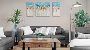 Una sala de estar moderna con un sofá gris, una mesa de centro de madera y tres cuadros abstractos en la pared.