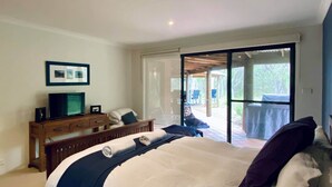 A bedroom with a large bed, a wooden dresser, a television, and a sliding glass door leading to an outdoor patio. - La Block Yallingup simply the best! (Yallingup)